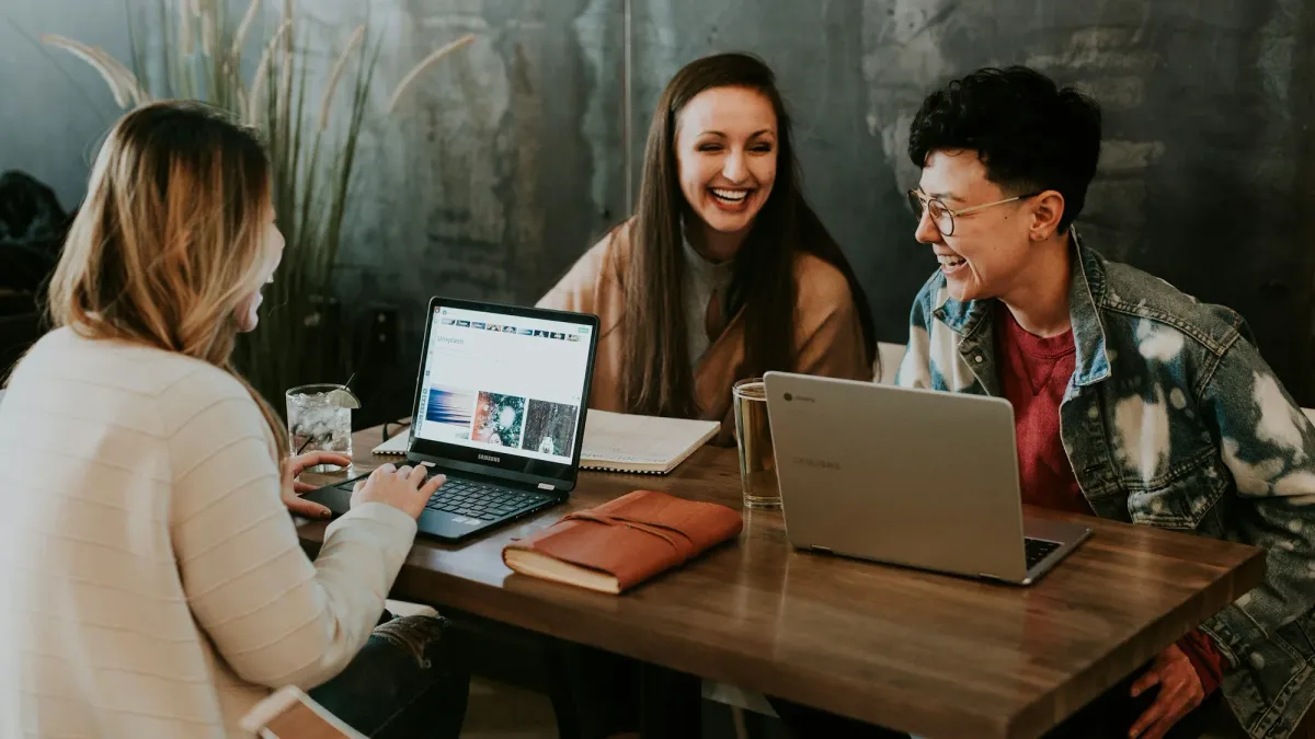 Three people working on laptops together at a cafe table
