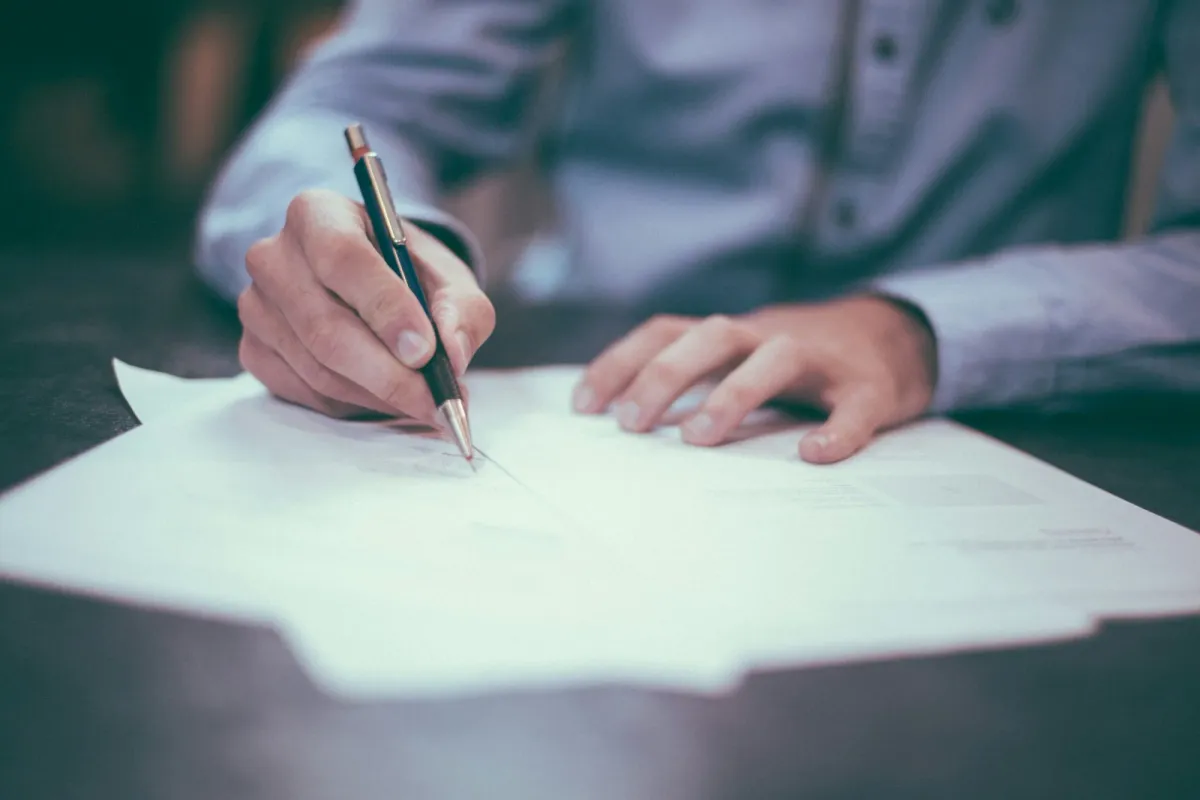 Close-up of hands writing on paperwork at a desk with a pen