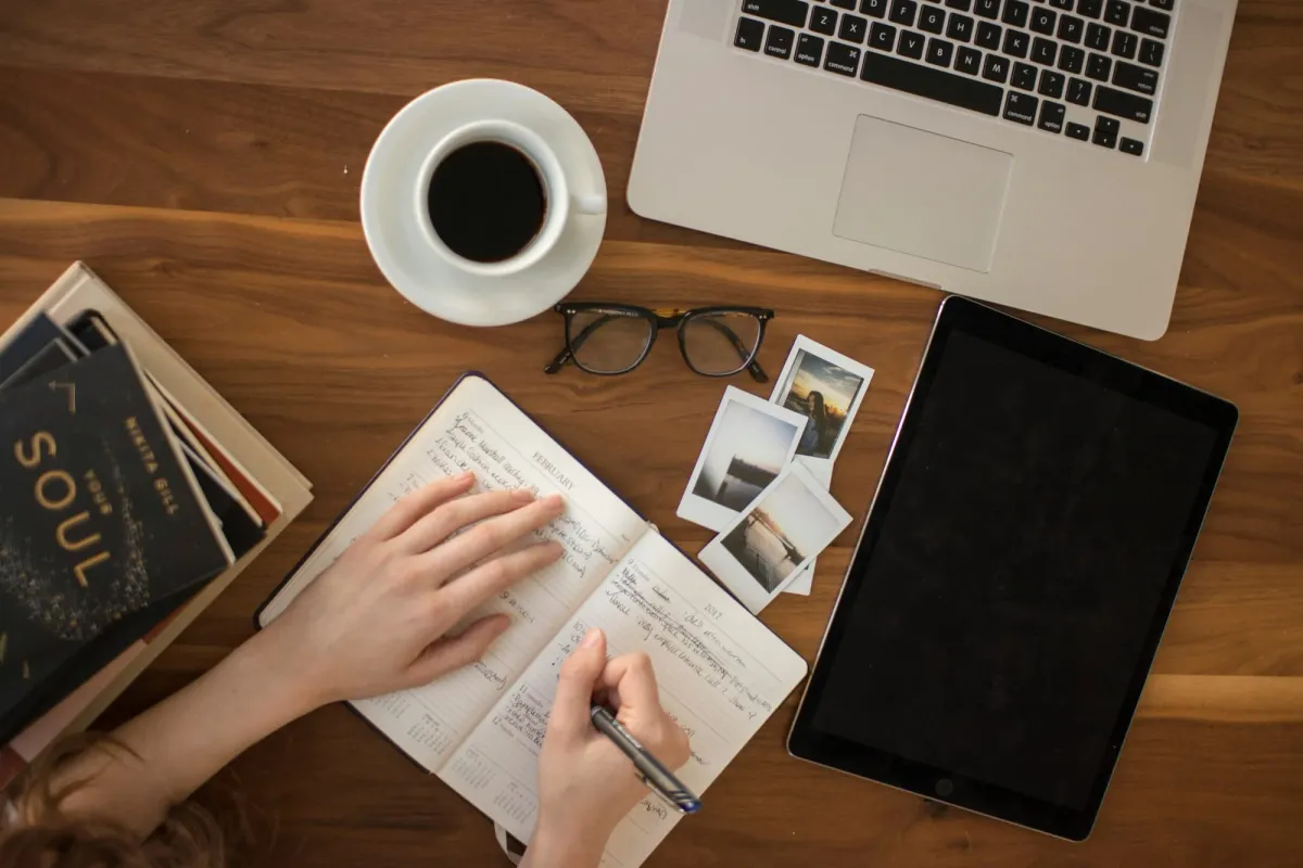 Hands planning in a journal beside a laptop and coffee, freelance web3 work