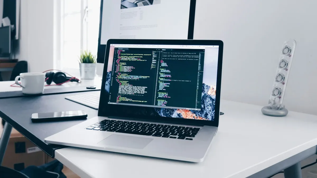 Laptop showing code on a tidy white desk with a lamp
