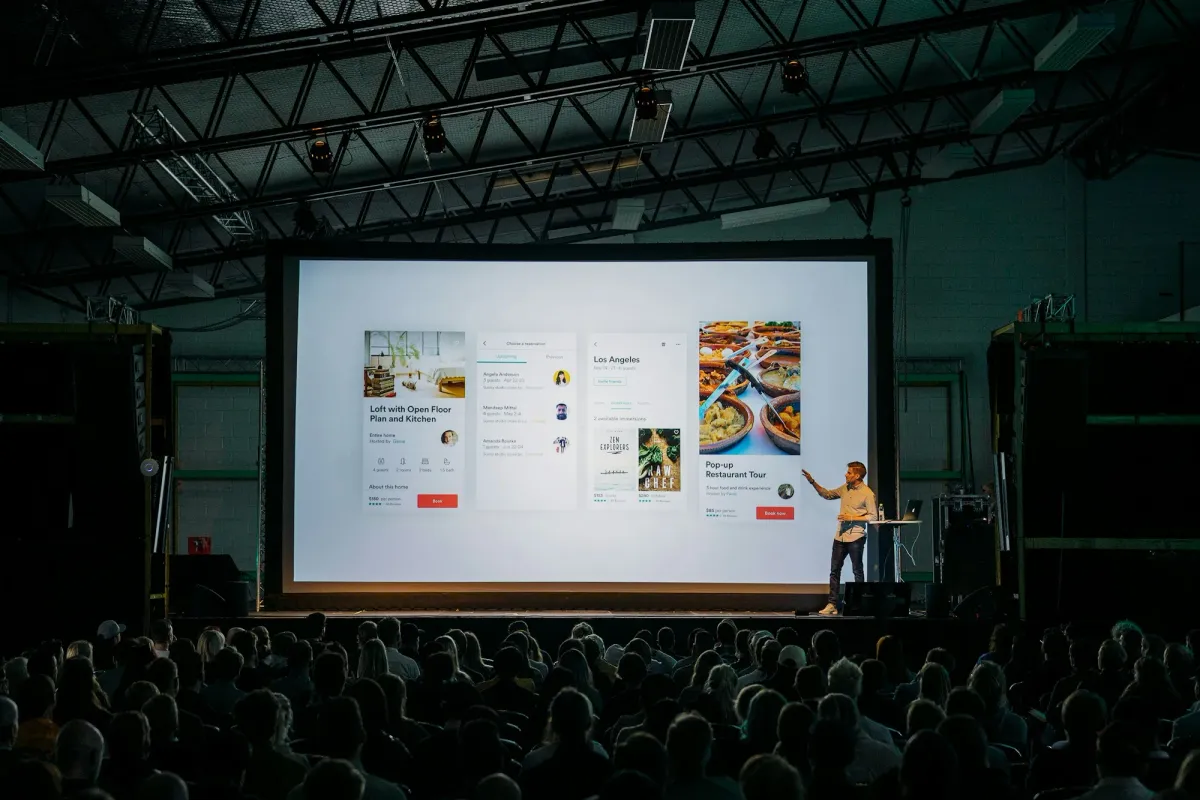 Speaker presenting beside a large screen at a developer conference