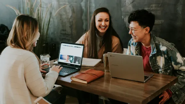 Three people working on laptops together at a cafe table