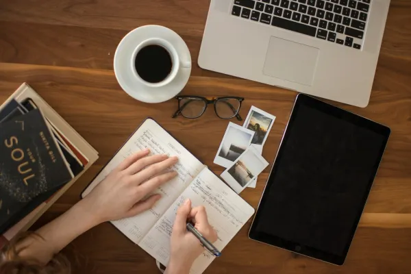 Hands planning in a journal beside a laptop and coffee, freelance web3 work