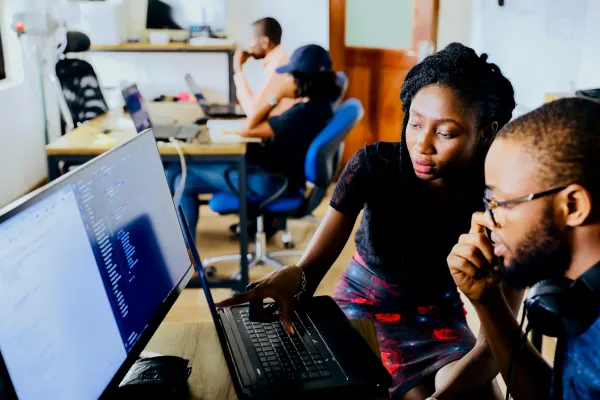 Two developers reviewing code together on monitors in a dark office