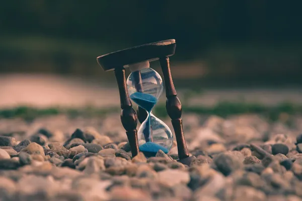 Hourglass with blue sand standing on pebbles at sunset